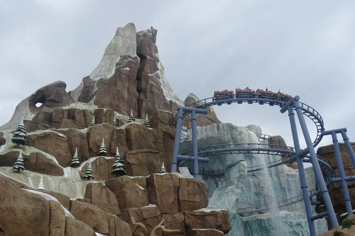 Roller coaster train curving past a rocky snow-capped mountain at Genting SkyWorlds