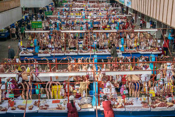 Indoor view of a bustling meat market in Almaty, showcasing rows of stalls with fresh cuts of meat, local vendors, and customers engaging in trade.