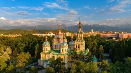 A beautiful church in Almaty, Kazakhstan, set against a backdrop of majestic mountains and modern city architecture, showcasing the city's cultural and architectural charm.