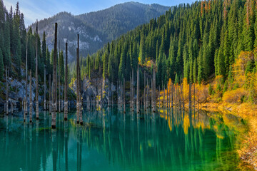 Stunning view of Candy Lake near Almaty, showcasing turquoise waters surrounded by dense evergreen forests and rugged mountain peaks, offering a serene and picturesque natural retreat.