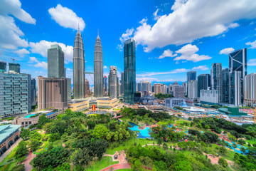 Vibrant daytime view of Petronas Twin Towers Malaysia, surrounded by lush greenery of KLCC Park and the modern skyline of Kuala Lumpur.