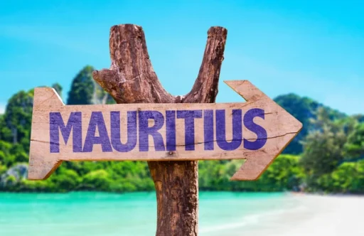 A wooden signpost with the word "Mauritius" pointing towards a beautiful tropical beach with clear blue water and lush greenery in the background. Best place to visit Mauritius