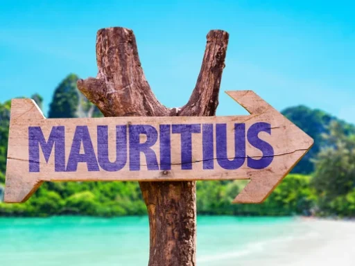 A wooden signpost with the word "Mauritius" pointing towards a beautiful tropical beach with clear blue water and lush greenery in the background. Best place to visit Mauritius