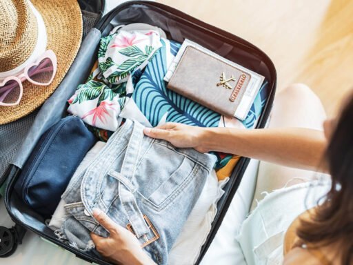 A woman is packing her bags for a trip. Image showing suitcase, hat and other accessories related to trip. While image is related to singapore tour package.