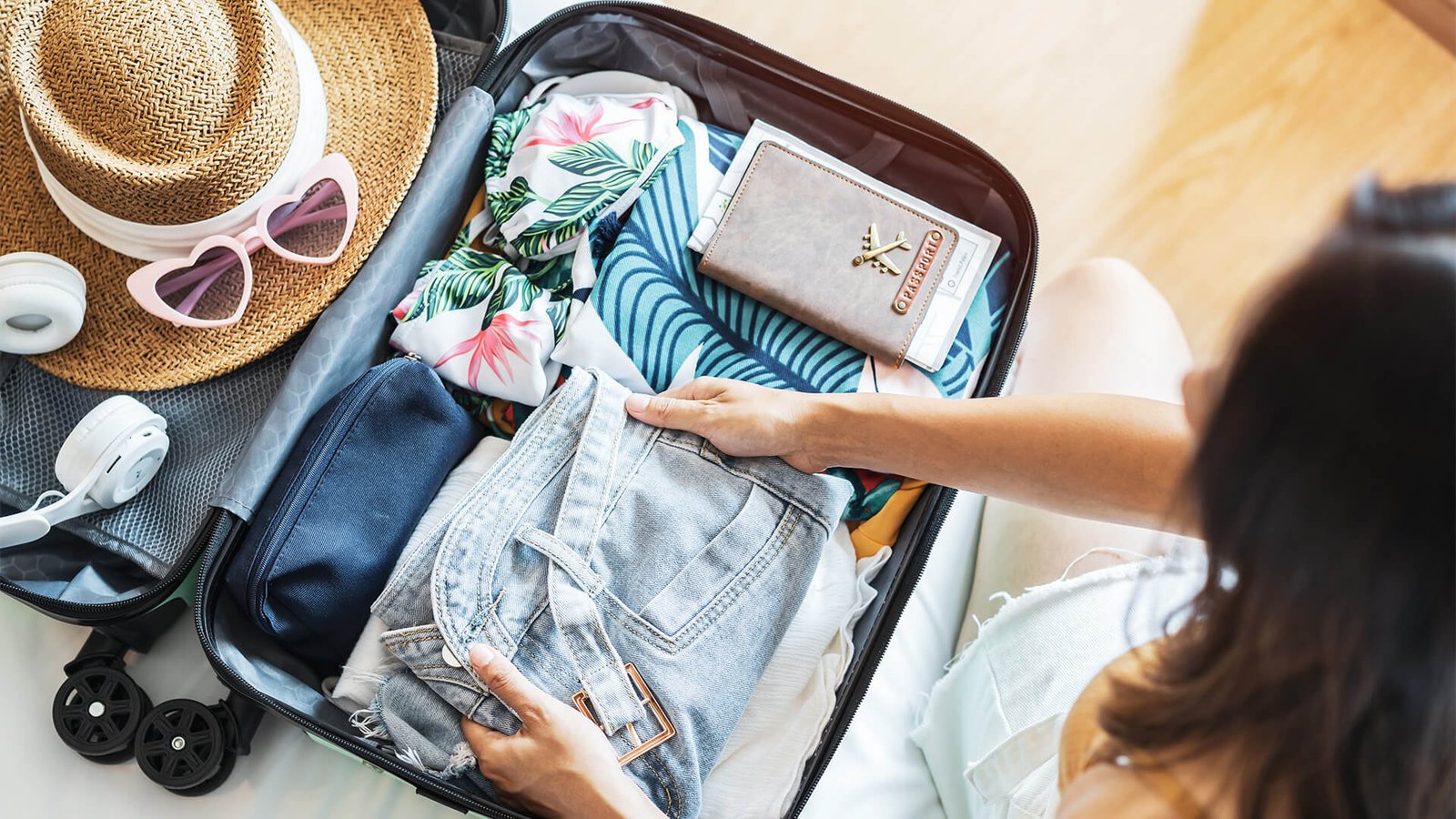 A woman is packing her bags for a trip. Image showing suitcase, hat and other accessories related to trip. While image is related to singapore tour package.