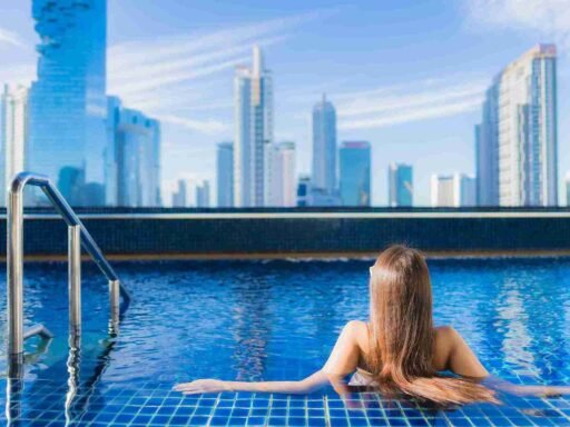 A woman relaxing at a rooftop pool with a panoramic view of city skyscrapers, representing the serene and luxurious experience at one of the best luxury hotels in Malaysia.