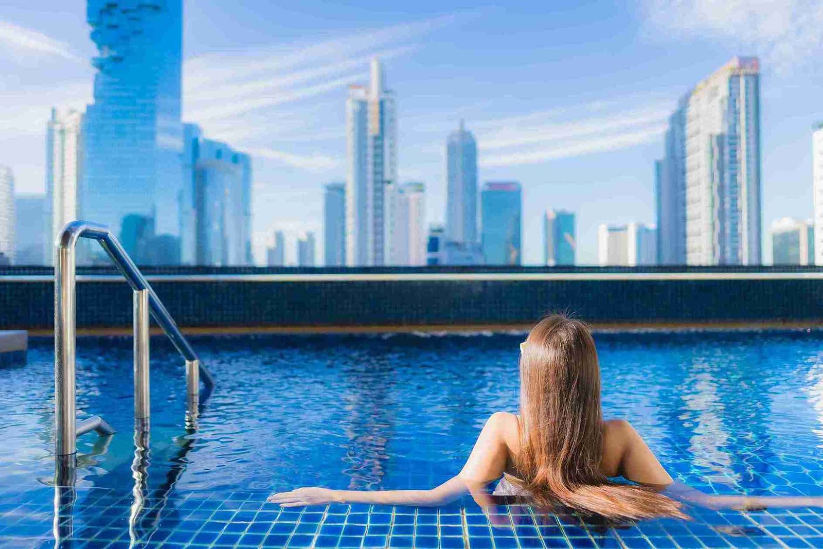 A woman relaxing at a rooftop pool with a panoramic view of city skyscrapers, representing the serene and luxurious experience at one of the best luxury hotels in Malaysia.