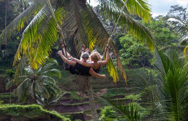 "Two travelers enjoying a thrilling jungle swing amidst lush greenery and terraced rice fields in Bali, showcasing the island's unique adventure activities in Bali