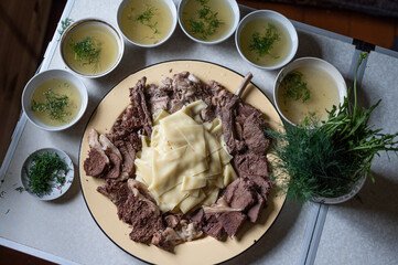 A traditional plate of Beshbarmak, the national dish of Kazakhstan, featuring tender boiled meat atop handmade noodles, garnished with fresh herbs and onion slices, surrounded by vibrant spices and ingredients on a rustic table."