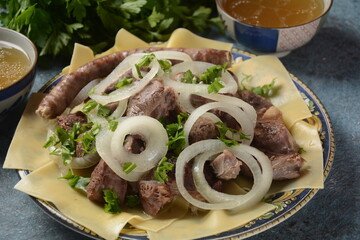 A traditional plate of Beshbarmak, the national dish of Kazakhstan, featuring tender boiled meat atop handmade noodles, garnished with fresh herbs and onion slices, surrounded by vibrant spices and ingredients on a rustic table."