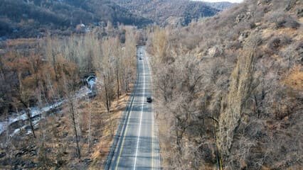 A bus traveling on a scenic mountain road surrounded by lush greenery and towering peaks route to Medeu Skating Rink in Almaty. 