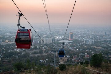 Scenic view of cable cars ascending Kok Tobe Hill Almaty at sunset, with panoramic city views and mountains in the background, highlighting the iconic attraction of Kazakhstan."