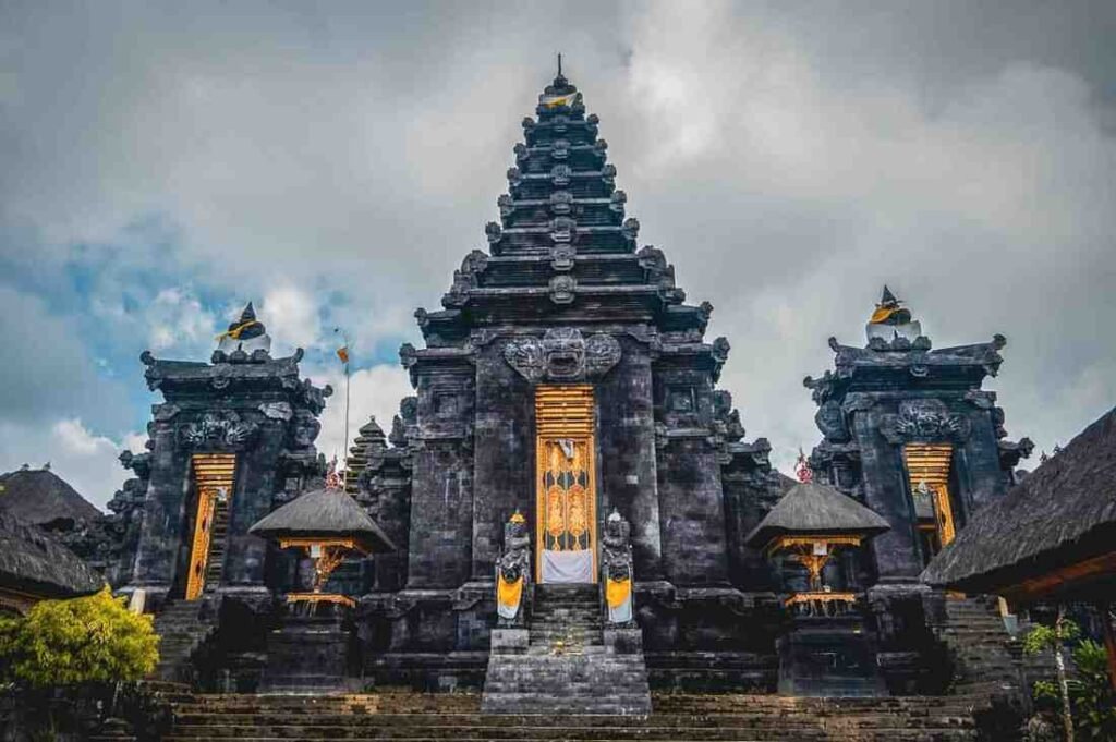 pura Besakih, the largest and holiest temple in Bali, featuring intricate architecture, gold accents, and a cloudy sky in the background.