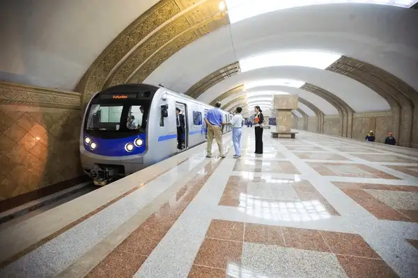 Almaty Metro station with passengers waiting or walking, showcasing the modern architecture and design of the metro, with individuals observing or standing near the platform.