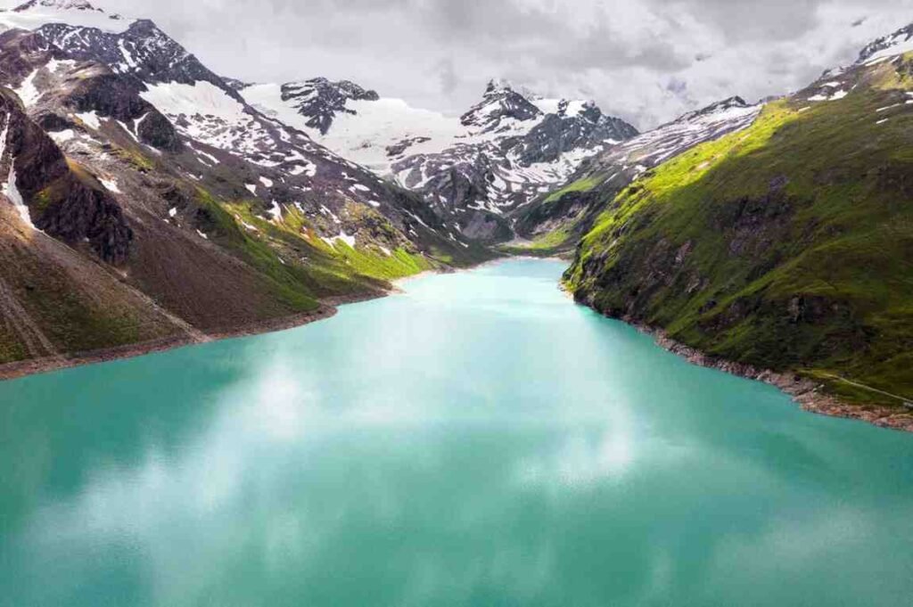 clear turquoise water of Big Almaty Lake with snow-capped peaks of the Tian Shan Mountains in the background, showcasing the pristine beauty of the landscape