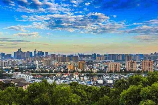 A scenic cityscape of Almaty with a mix of high-rise buildings and traditional architecture, lush greenery in the foreground, and a vibrant blue sky with scattered clouds. Perfect for exploring the best things to do in Almaty, from urban sightseeing to nature excursions.