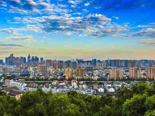 A scenic cityscape of Almaty with a mix of high-rise buildings and traditional architecture, lush greenery in the foreground, and a vibrant blue sky with scattered clouds. Perfect for exploring the best things to do in Almaty, from urban sightseeing to nature excursions.