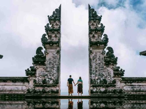 A young couple standing at the iconic Gates of Heaven at Lempuyang Temple in Bali, Indonesia, holding hands, with a cloudy sky in the background. Image Source: FreePik