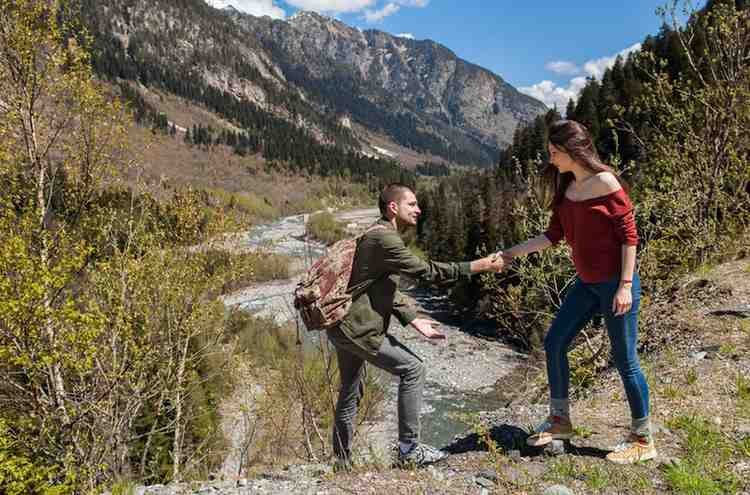 A couples hiking Big Almaty Lake, surrounded by snow-capped mountains and forest, enjoying the breathtaking natural beauty of the Tian Shan Mountains