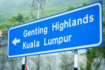 A directional road sign pointing towards Genting Highlands and Kuala Lumpur, surrounded by lush greenery and misty hills, symbolizing a scenic journey in Malaysia.