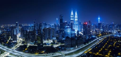 This image showcases a stunning night view of Kuala Lumpur, Malaysia, featuring the iconic Petronas Twin Towers illuminated against the city skyline. The dazzling highways and vibrant cityscape highlight the modern attractions of Malaysia. It beautifully represents the "Top Attractions of Malaysia