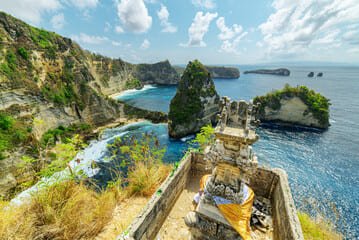 Panoramic view of Nusa Islands Bali featuring dramatic coastal cliffs, azure waters, and a traditional Balinese shrine overlooking the stunning seascape.