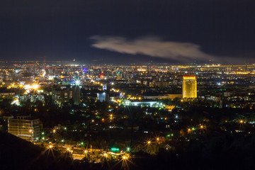 Nighttime panorama of Alma-Ata City illuminated with vibrant city lights, showcasing its lively urban atmosphere and stunning skyline against the dark sky.