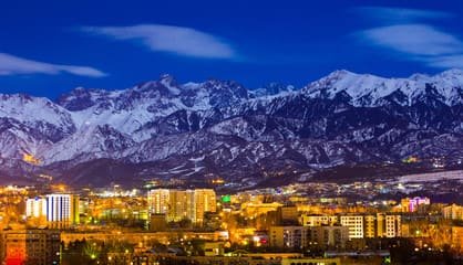 Scenic view of Almaty with Soviet-era architecture, tree-lined streets, and majestic mountains in the background, showcasing the city's charm.