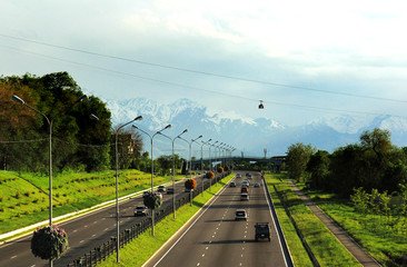 A serene highway in Almaty, lined with greenery and framed by the majestic Tian Shan Mountains, showcasing travel experiences.