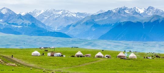 A scenic highway in Almaty surrounded by lush greenery, with snow-capped mountains in the background, showcasing the tranquility of off-peak travel.