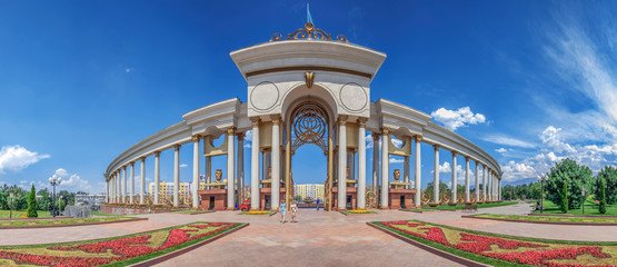 A stunning wide-angle view of the First President's Park in Almaty, Kazakhstan, featuring its grand archway, elegant columns, vibrant flower arrangements, and clear blue skies. An iconic landmark for visitors exploring Almaty's beauty and cultural significance. Keywords: Travel to Almaty Kazakhstan.