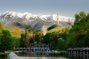 Scenic view of Almaty, Kazakhstan, showcasing snow-capped mountains, Kok Tobe Tower, lush greenery, and serene water—Arriving in Almaty.