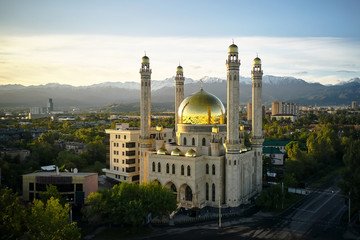 Scenic view of Almaty's golden-domed Central Mosque with the Tian Shan Mountains in the background, highlighting the charm of 'Almaty on a Budget' for  cultural exploration.