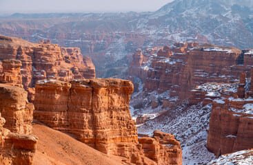 Charyn Canyon, located in Kazakhstan, showcasing a breathtaking landscape of towering red rock formations and deep valleys, illuminated by the warm glow of the setting sun.