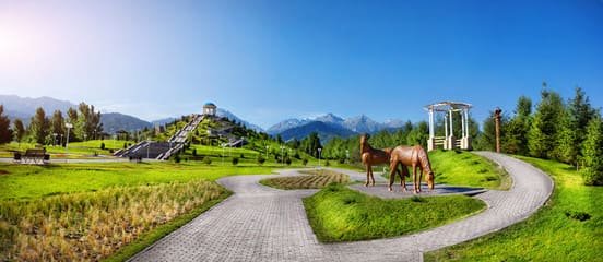 Beautiful park in Almaty with a scenic pathway, lush greenery, stunning mountain views, and artistic horse sculptures.