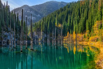 Stunning view of Candy Lake near Almaty, showcasing turquoise waters surrounded by dense evergreen forests and rugged mountain peaks, offering a serene and picturesque natural retreat.