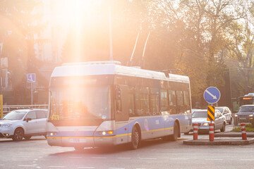 City bus bathed in warm sunlight, navigating urban streets with cars in the background, highlighting a serene city commute scene.