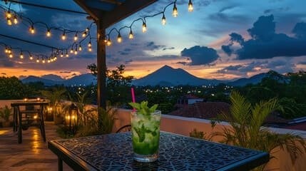 A refreshing cocktail on a rooftop table in Almaty, with string lights, mountain views, and a stunning sunset, showcasing the charm of Almaty’s rooftop bars.