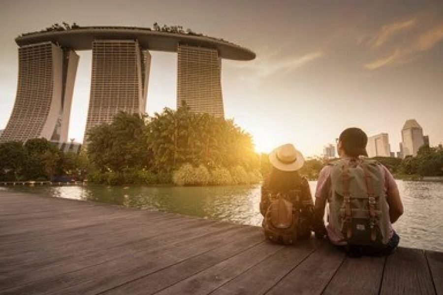 A couple sitting by the waterfront, enjoying a serene sunset view of Marina Bay Sands in Singapore, surrounded by lush greenery and iconic cityscape.