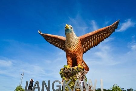 A majestic eagle statue at Dataran Lang (Eagle Square) in Langkawi, Malaysia, with its wings spread wide against a clear blue sky. The large 