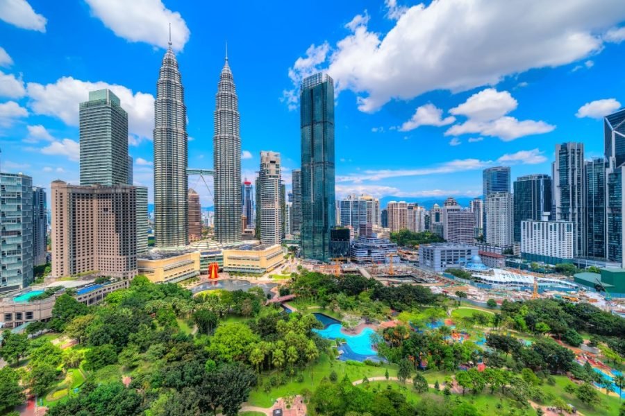 Panoramic view of Kuala Lumpur showcasing the iconic Petronas Twin Towers surrounded by modern skyscrapers, lush greenery, and vibrant city parks under a bright blue sky.